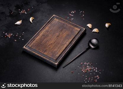 Black metal spoon and rectangular cutting board on black concrete background. Preparing for Cooking. Black metal spoon and rectangular cutting board on black concrete background