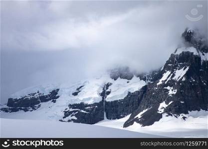 Black mountains covered by snow and clouds with great lighting in Antarctica