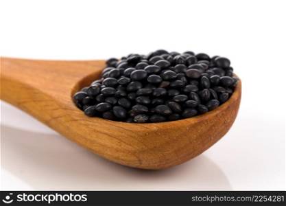Black organic lentils in wooden spoon isolated on white background