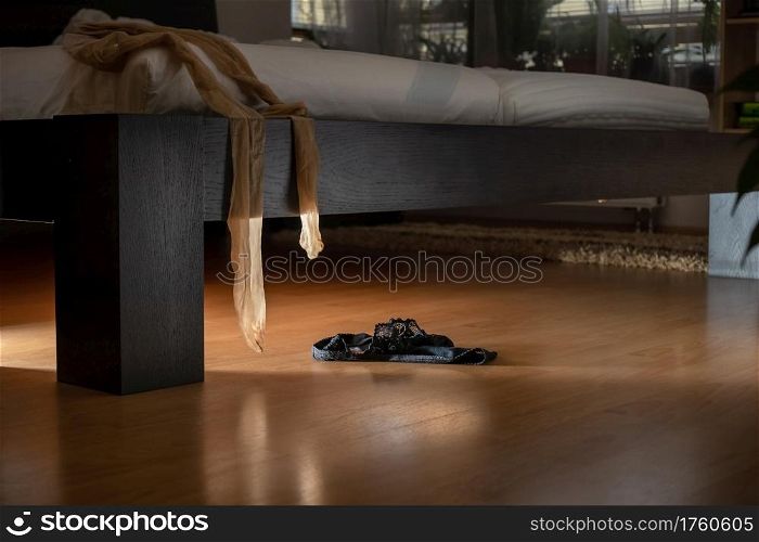 Black panties lying on the floor and stockings hanging from a bed in a dark room