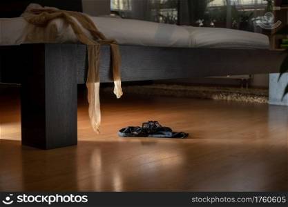 Black panties lying on the floor and stockings hanging from a bed in a dark room