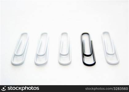 Black paper clip standing out from group of white ones.