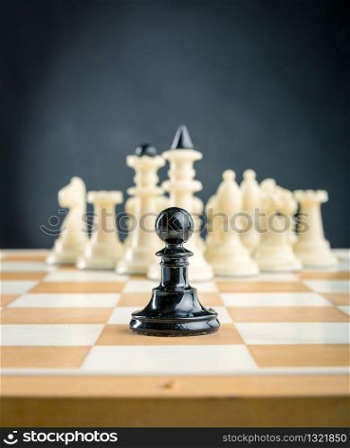 Black pawn standing in front of the white chess team. Chess figures