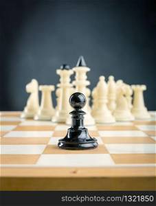 Black pawn standing in front of the white chess team. Chess figures