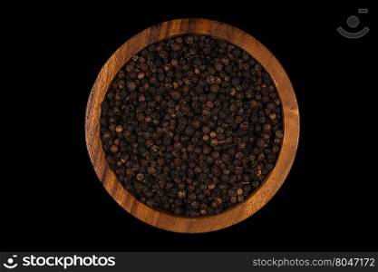 Black pepper in wooden bowl on dark stone background