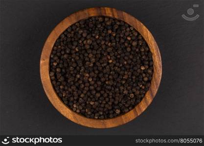 Black pepper in wooden bowl on dark stone background