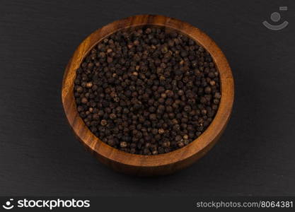 Black pepper in wooden bowl on dark stone background