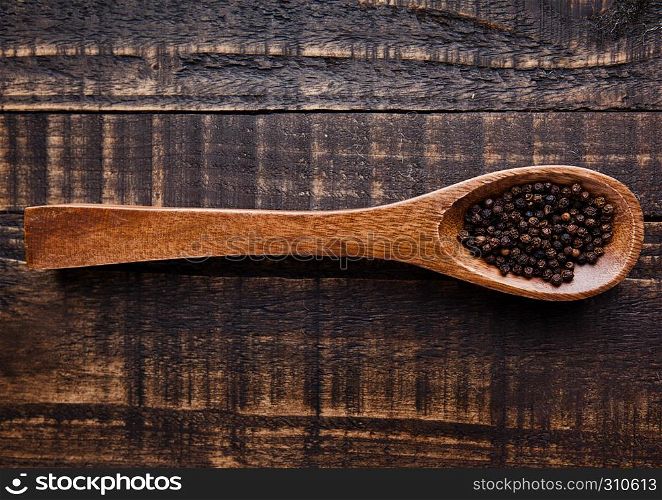 Black pepper on wooden spoon on grunge background. Kitchen equipment