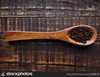 Black pepper on wooden spoon on grunge background. Kitchen equipment
