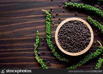 Black pepper seeds in a cup are placed on an old wooden table.