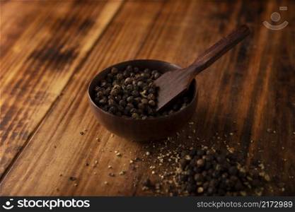 Black pepper seeds in a small wooden bowl on a rustic wooden table. Close up