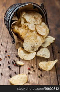 Black pepper taste potato crisps chips in steel snack bucket on wooden background. Top view