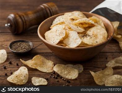 Black pepper taste potato crisps chips in wooden bowl bucket on wooden table background with mill and ground pepper with package.