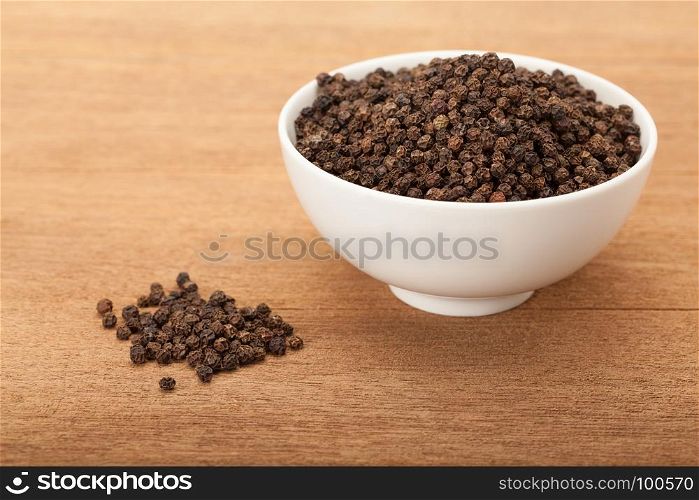 black peppercorns in white ceramic bowl on wood background