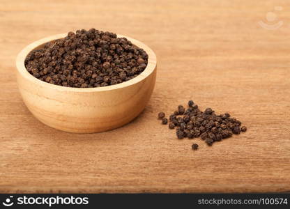 black peppercorns in wooden bowl on wood background