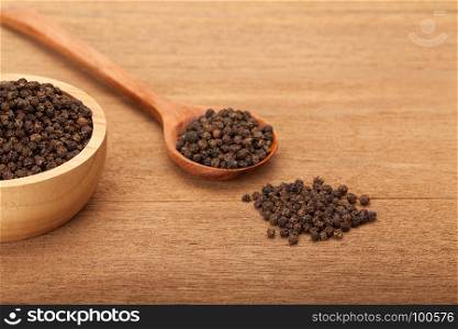 black peppercorns in wooden bowl on wood background