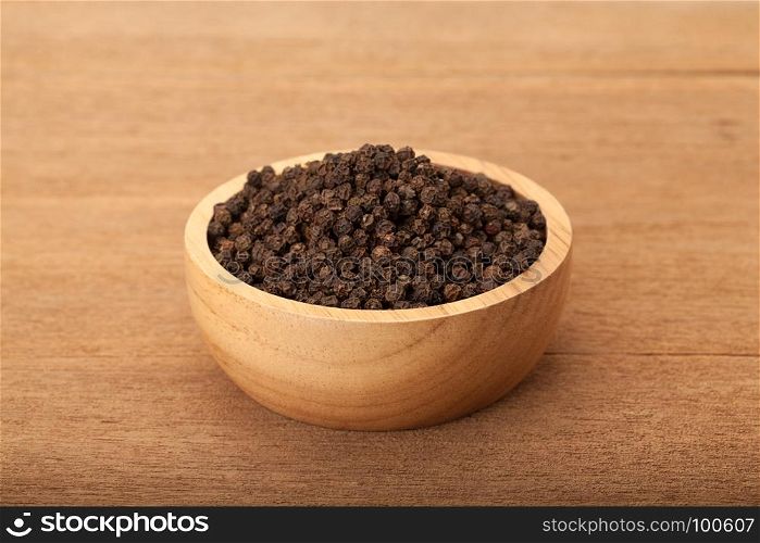 black peppercorns in wooden bowl on wood background