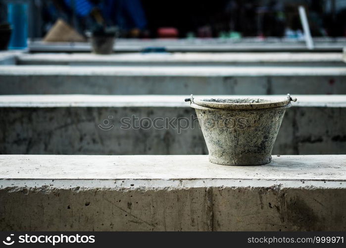 Black plastic bucket filled with cement water stains. Placed on a large concrete beam. On site construction, selective focus.