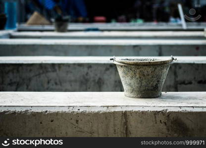 Black plastic bucket filled with cement water stains. Placed on a large concrete beam. On site construction, selective focus.