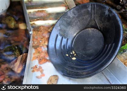 Black plastic gold pan with 6 gold nuggets inside a sluice box with some water flowing through it.. Gold Pan And Nuggets