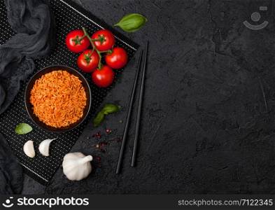 Black plate bowl of rice with tomato and basil and garlic and chopsticks on black background. Space for text