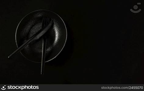 Black plate in the japanese style with fork and knife, table setting. Flat lay. Black background, top view with copy space. Minimalist breakfast idea in black color.