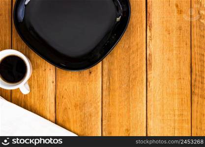 Black plate, white napkin and cup of coffee over wooden table, top view, copy space. Breakfast concept