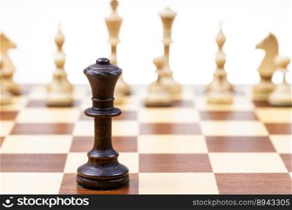 black queen against white chess figures in background on wooden chessboard close up (focus on queen)
