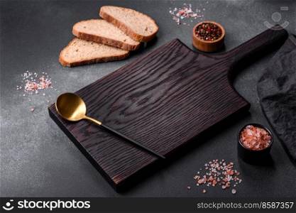 Black rectangular wooden cutting board with salt and spices on a dark concrete background. Cooking at home. Black rectangular wooden cutting board with salt and spices