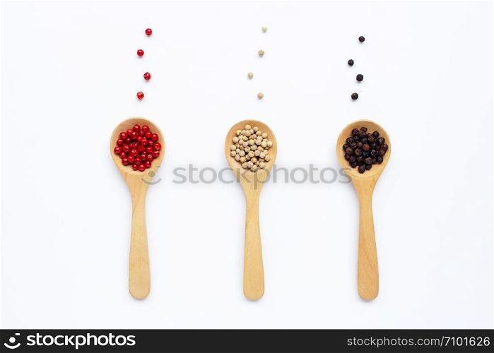 Black, red and white peppercorns with wooden spoon on white background.