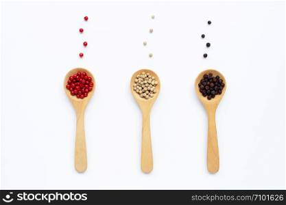 Black, red and white peppercorns with wooden spoon on white background.