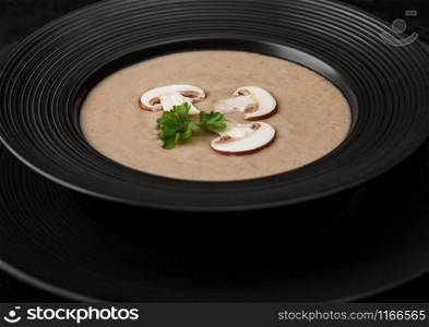 Black restaurant plate of creamy chestnut champignon mushroom soup on black background.