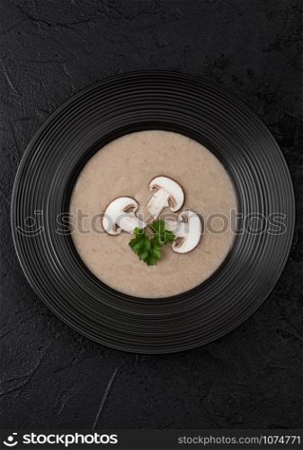 Black restaurant plate of creamy chestnut champignon mushroom soup on black background. Top view.