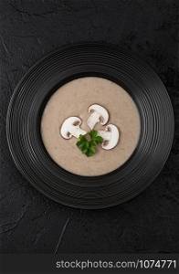 Black restaurant plate of creamy chestnut champignon mushroom soup on black background. Top view.