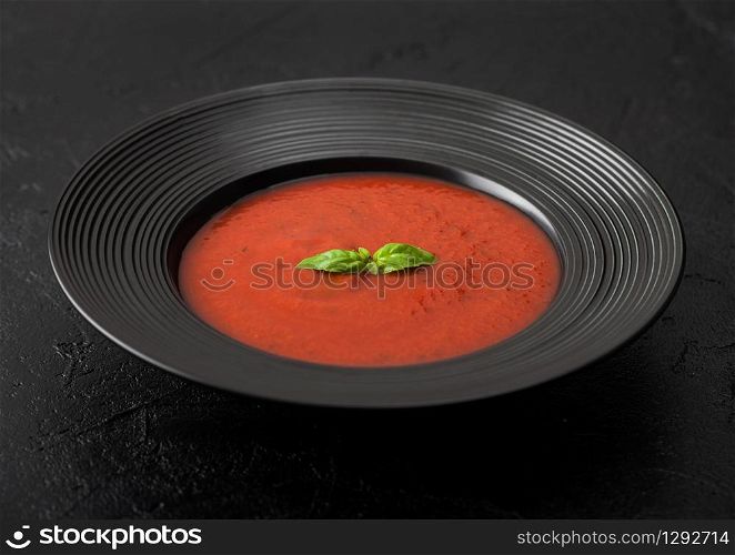 Black restaurant plate of creamy tomato soup on black background.