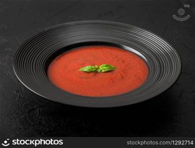 Black restaurant plate of creamy tomato soup on black background.