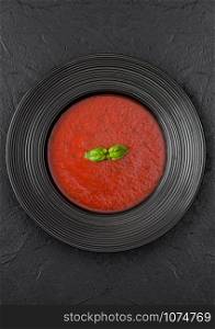 Black restaurant plate of creamy tomato soup on black background. Top view
