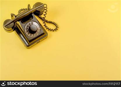 Black retro landline telephone on yellow background.