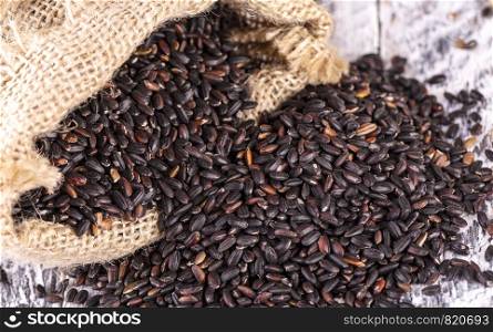 black rice and a bag of burlap on old wooden background