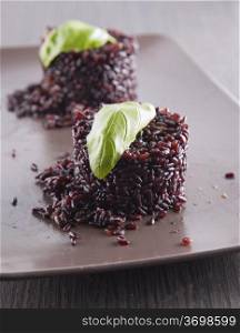 "Black rice type "Venere" over brown plate with basil leaf"