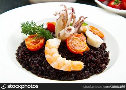 Black rice with sliced squids ,prawns and tomato on white plate