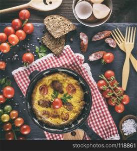 black round frying pan with fried omelette, whipped eggs with cherry tomatoes, top view