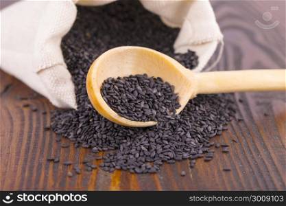 black sesame in spoon and bag on wooden surface