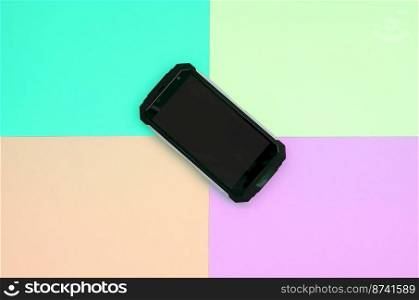 Black shock-proof smartphone lies on a pastel colored background. Modern technology concept. Minimalism flat lay. Blue, peach, lime and purple pastel colors. Black shock-proof smartphone lies on a pastel colored background