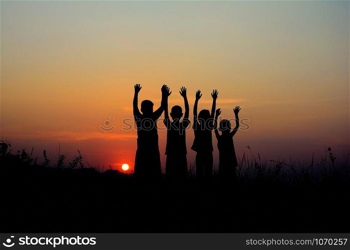 Black silhouette of four children standing together. There is a sky at sunset background