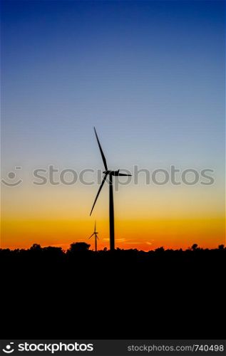 Black silhouette of wind turbines against blue and orange sky at dusk.