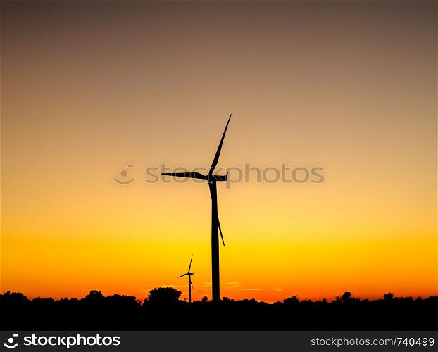 Black silhouette of wind turbines against orange sky at dusk.