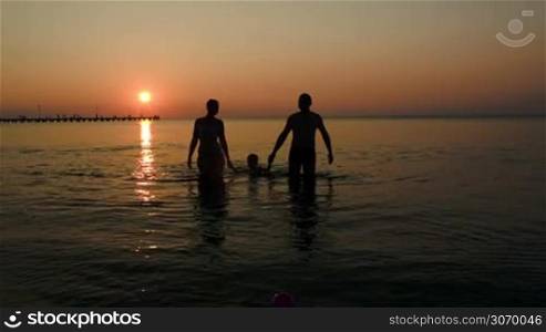 Black silhouettes of parents and son holding hands and coming out of sea at sunset
