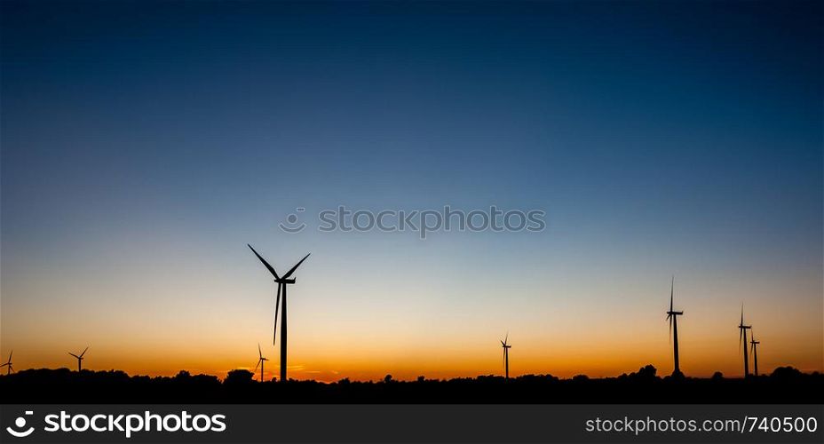 Black silhouettes of several wind turbines against orange and blue sky at dusk.