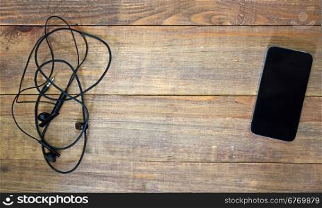 black smart phone and earphones on wooden background